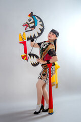 A traditional Javanese Jathilan dancer holds a flat horse puppet, wearing a vibrant costume with...