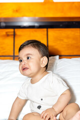Baby sitting in bed and leaning on his right hand looking to do something else
