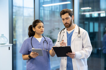 Two medical professionals review a patient's charts. One holds a tablet, and the other uses a clipboard. They appear focused and engaged in their discussion.