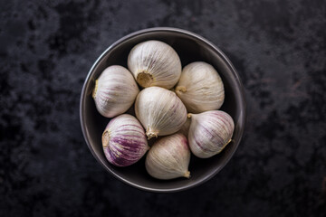 Solo glove garlic bulbs in bowl on black table. Top view.