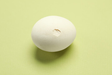 One egg with cracked shell on light green background, above view