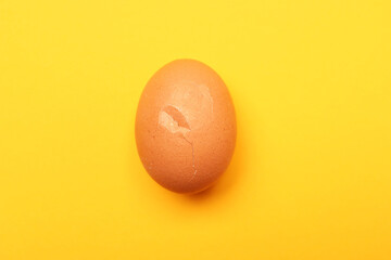 One egg with cracked shell on yellow background, top view