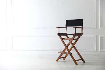 One empty director's chair near white wall indoors, space for text