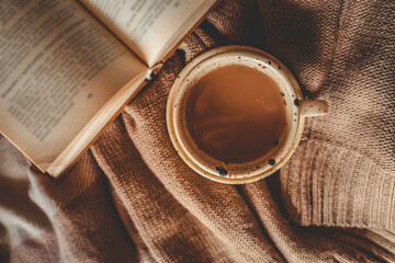 Top view of a speckled ceramic mug with tea or coffee placed on a cozy brown knitted blanket next...
