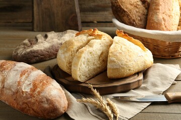 Different loaves of fresh bread, knife and spikes on wooden table