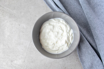 Gray bowl with white natural yogurt on the stone marble table.