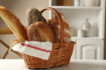Different loaves of fresh bread and spikes in wicker basket on white wooden table indoors