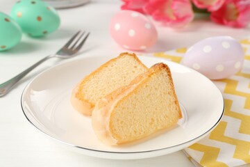 Pieces of delicious bundt cake, Easter eggs and tulips on white wooden table, closeup