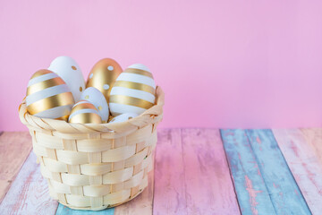 A wooden basket filled with decorated easter eggs on a pink background