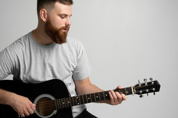Bearded brunette man with a guitar in hands playing a song.