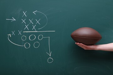 Man holding American football ball near chalkboard with scheme of game, closeup