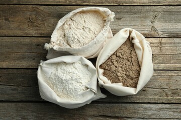 Different types of flour in bags on wooden table, flat lay