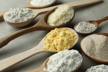 Different types of flour in spoons on light grey table, closeup