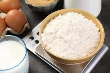 Digital kitchen scale with bowl of flour and other products on grey table, closeup