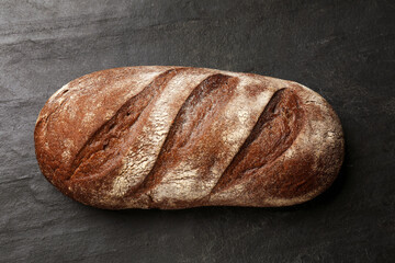 Fresh loaf of bread on black table, top view