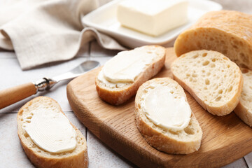 Pieces of bread with butter and knife on light tiled table, closeup