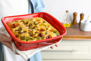 Woman holding delicious focaccia with vegetables and olives in kitchen, closeup