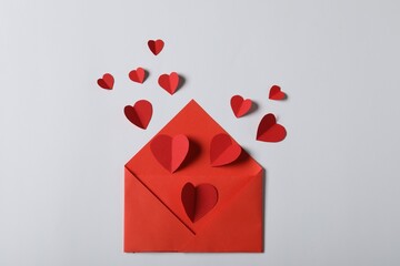 Many paper hearts flying out of envelope on light grey background, flat lay