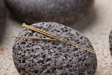 Acupuncture needles and spa stones on light textured table, closeup
