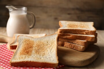 Slices of tasty toasted bread and jug of milk on wooden table, closeup
