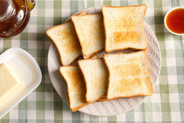 Slices of tasty toasted bread, butter and jam on checkered tablecloth, flat lay
