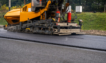 Asphalt paver machine laying fresh asphalt on road construction site.