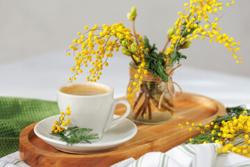 A fresh cup of espresso on a wooden tray, surrounded by mimosa flowers in a glass jar, bringing a springtime charm.