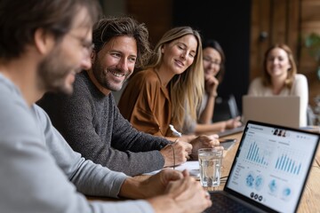 Smiling team members share ideas around a table, focused on a laptop screen in a bright office.