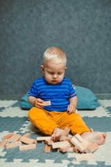Fototapeta premium Toddler boy in a T-shirt and pants playing with toys at home. Children's home clothes. Child's self-development at home.