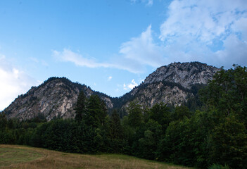 Breathtaking peaks tower over lush greenery, as clouds dance across the brilliant blue sky in Germanys countryside.