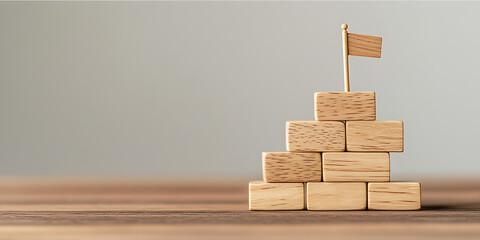 Wooden block tower with flag represents goals and success, achieved step by step. Strategy and planning are key for accomplishment.