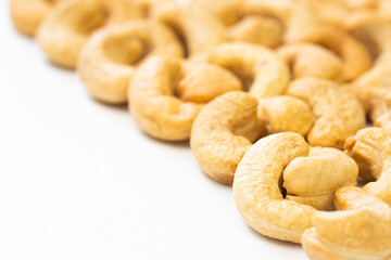 Naklejka premium Close-up of roasted cashew nuts in a curved row on a white background with soft focus, ideal for food, health, and nutrition-related concepts or designs.