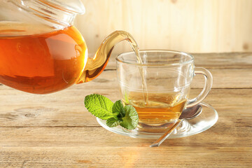 Pouring freshly brewed tea from teapot into glass cup on wooden table, closeup