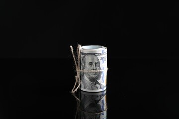 Rolled dollar banknotes with rope on dark mirror surface