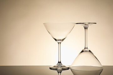 Two empty clean glasses on mirror surface against beige background. Space for text