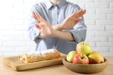 Woman refusing to eat products at wooden table near white brick wall, selective focus. Food allergy concept