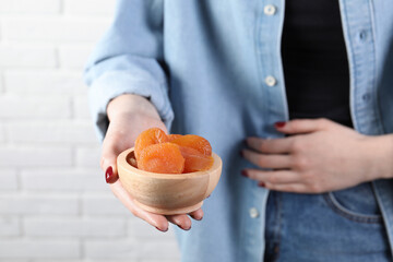 Woman refusing to eat dried apricots near white brick wall, closeup. Food allergy concept