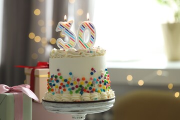 30th birthday. Tasty cake with burning number shaped candles, sprinkles and gift boxes on blurred background with lights, space for text. Bokeh effect