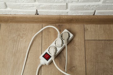 Extension power board overloaded with plugs on wooden floor, above view