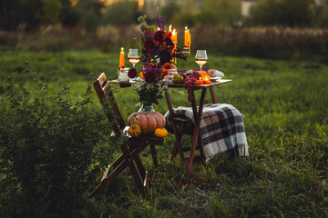 Beautiful elegant autumn table setting for thanksgiving family dinner or wedding. Orange pumpkin with flowers as centrepiece. Cozy fall home atmosphere. Wineglass, romantic marriage proposal, sunset
