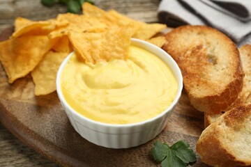 Tasty cheese dipping sauce in bowl, nacho chips and croutons on table, closeup