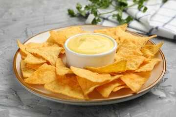 Tasty cheese dipping sauce in bowl, nacho chips and parsley on grey table, closeup
