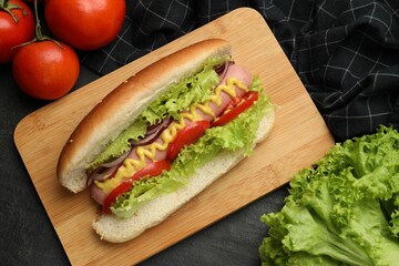 Tasty hot dog with vegetables on black table, flat lay