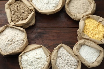 Frame of different flour types in paper bags on wooden table, flat lay. Space for text