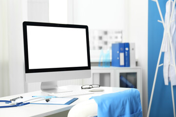 Doctor's workplace. Computer monitor, clipboard, stethoscope and glasses on white table in medical office