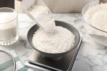 Woman putting sugar into bowl on digital kitchen scale at white marble table, closeup