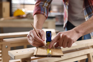 Man measuring wooden plank with tape and pencil indoors, closeup