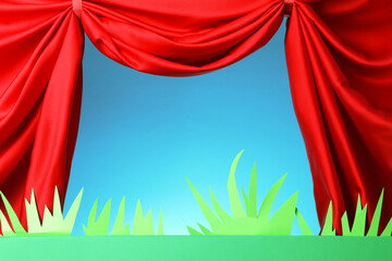 Puppet show. Empty green stage with decorations and red curtains against light blue background