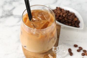Tasty iced coffee and beans on white marble table, closeup