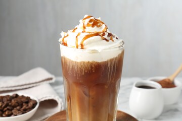 Tasty iced coffee with whipped cream, syrup and beans on white table, closeup